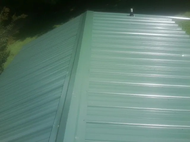 New green metal panels meeting at the ridge of a roof — Flat Roof Repair work by our crew in Centreville